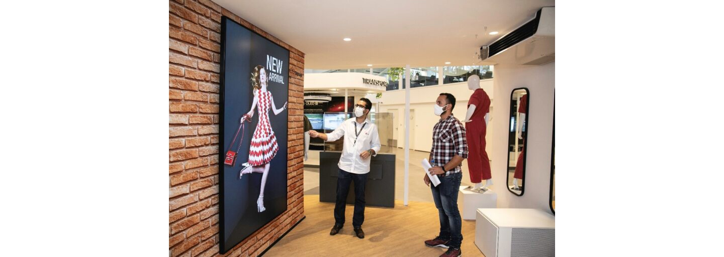 Two men admiring LG signage as it displays a fashion model in a white and red patterned dress.