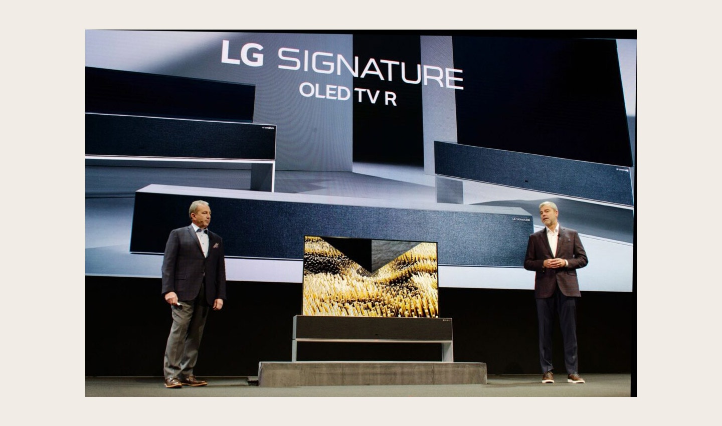 David VanderWall, Senior Vice President of Marketing at LG Electronics USA and Tim Alessi Senior Director of Product Marketing for Home Entertainment Products at LG Electronics USA are onstage discussing the LG SIGNATURE OLED TV R at LG's CES 2019 Press Conference while putting the TV between them.