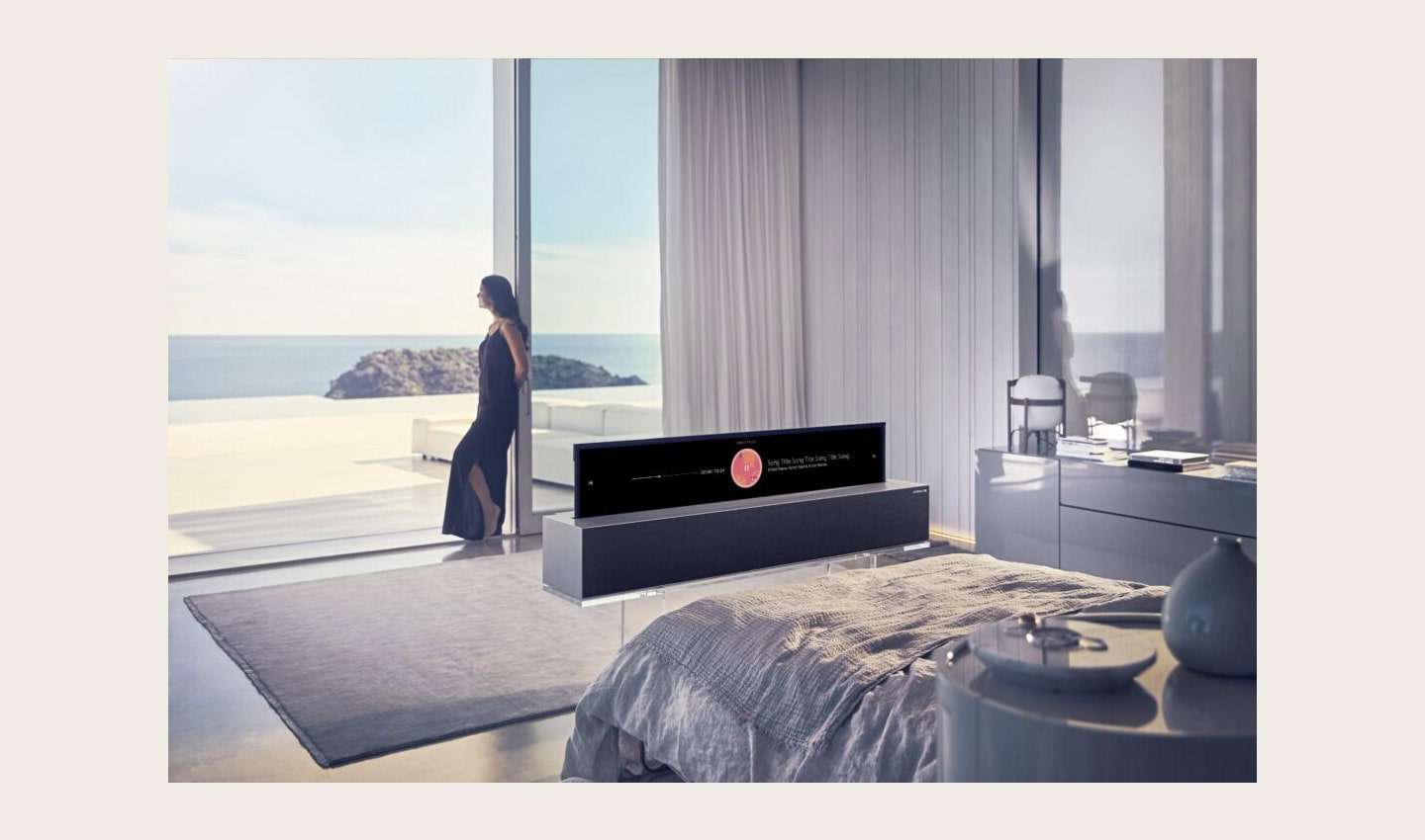 A woman looking out of the window while an LG SIGNATURE OLED TV R is at the foot of the bed displaying the music playlist.