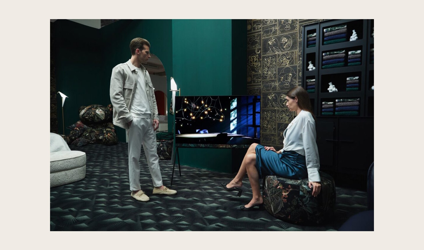 A man and woman admire the LG OLED Objet Collection Posé model in the center of a green-themed space designed by Dutch brand Moooi