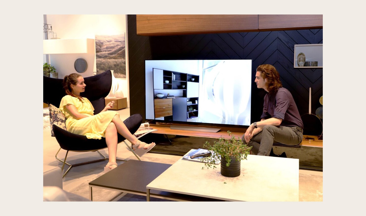 A man and a woman sit in the sample AI-enabled living room discussing LG's AI ThinQ-enabled TVs