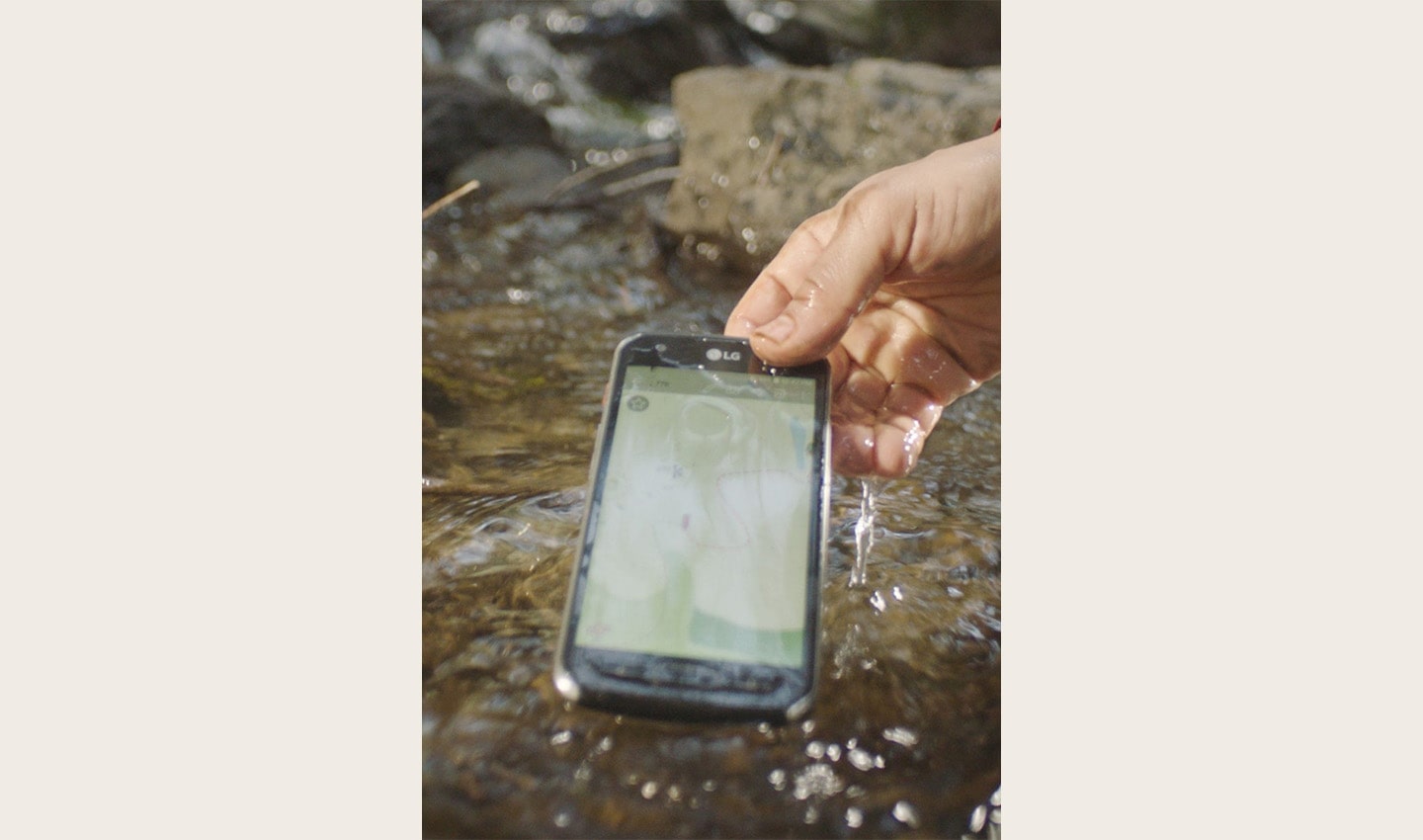A hand lifting the water-resistant LG X Venture smartphone from water, the phone is still turned on
