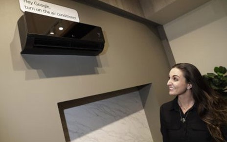 Woman looking up at a black LG air conditioner with a sign that says “Hey Google, turn on the air conditioner”