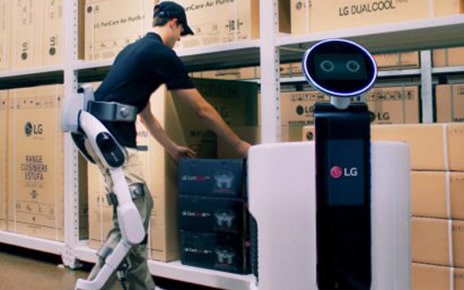 Man wearing LG CLOi SuitBot to move a box to the LG Shopping Cart Robot in a LG warehouse
