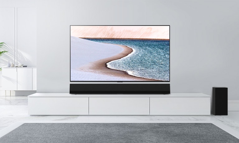 電視安裝在淺灰色牆壁上。LG Soundbar 放置在下方的白色櫃子。電視展示出一個海灘。