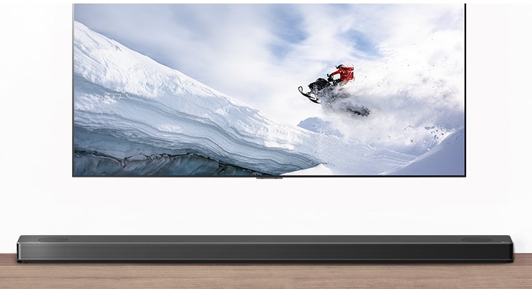 從正面看到的電視和 Soundbar。電視節目顯示男子在雪山騎雪上電單車。HDMI 2.1 標誌位於電視下方。