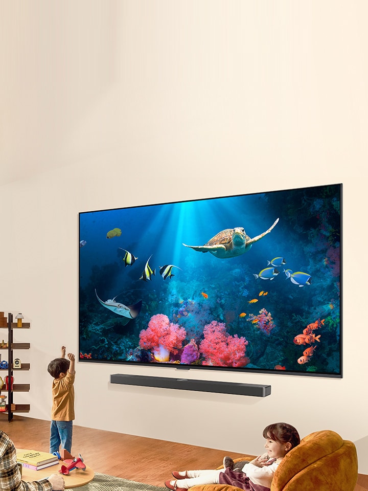 一家人正在明亮自然的生活空間中，透過 LG QNED 電視和 LG Soundbar 觀賞一個明亮的水下場景。