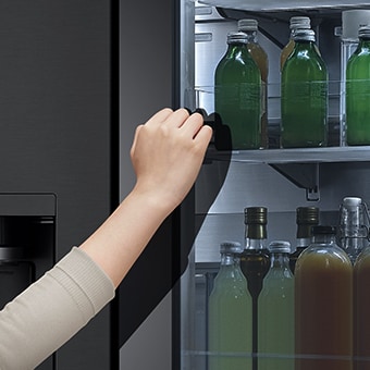 The front view of a black glass InstaView refrigerator with the light on inside. Hands tapping on InstaView screen.	