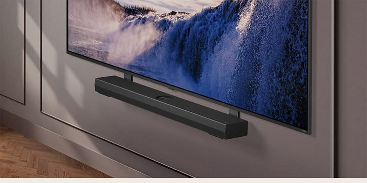 LG TV appears with a Synergy Bracket. The Synergy Bracket and LG TV are connected. The camera zooms in on the Synergy Bracket, revealing the soundbar, which is placed on top of the Synergy Bracket, followed by the background of a modern living space.	