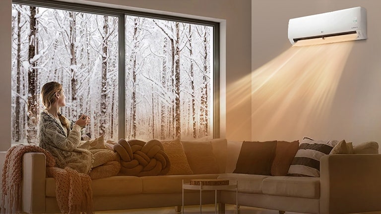 A woman sitting on a sofa in her house in the cold winter and warming up in the warm air conditioner wind.