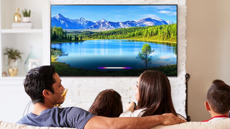 Family in bright living room viewing a landscape on wall-mounted TV