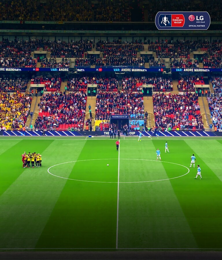 Wide shot of a soccer pitch. The players are gathering in the middle to prepare for the match.