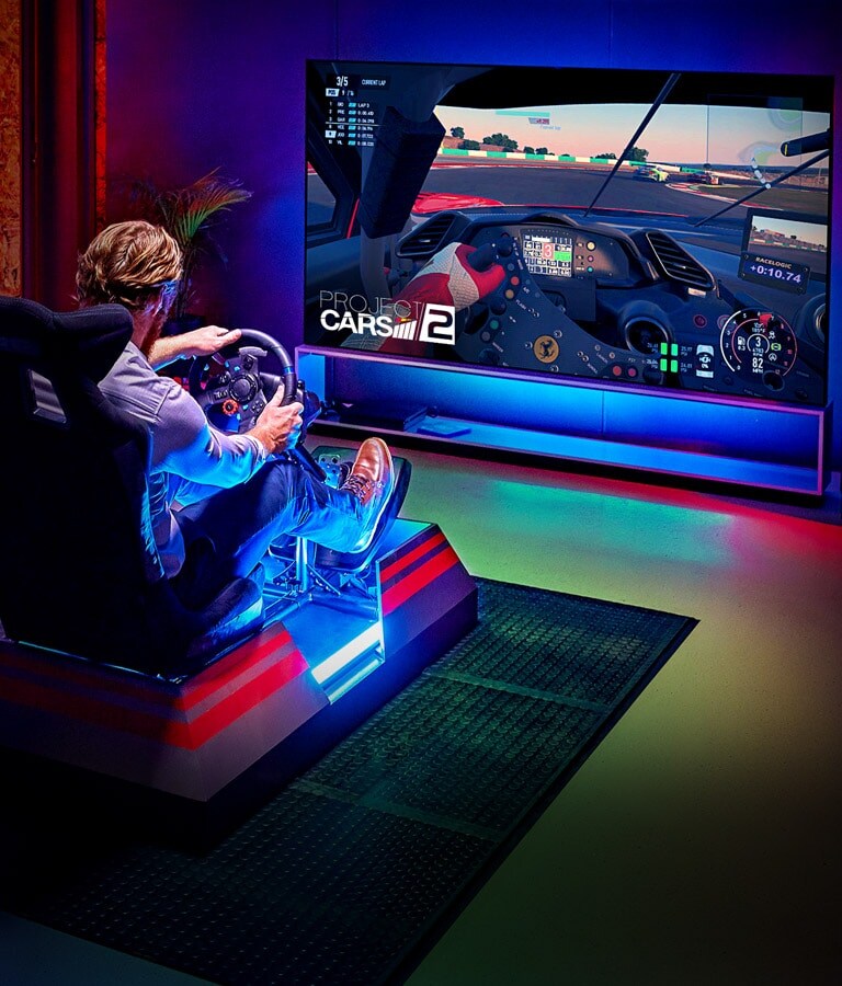 In front of a large LG OLED TV, a man is sitting on a racing seat and playing a racing game (scroll down the page)