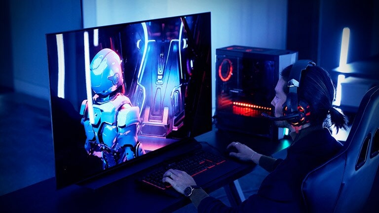 A man playing at gaming station set up with a 48-inch LG OLED TV CX, desk, and chair