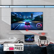 An LG OLED evo M4 mounted on a living room wall and a laptop on a table in front displaying the same car racing game. A close-up of a Zero Connect Box on a smaller table, with a console connected underneath and a red Wi-Fi signal and red beam emitting towards the TV. The words "hassle FREE" in the bottom left corner.
