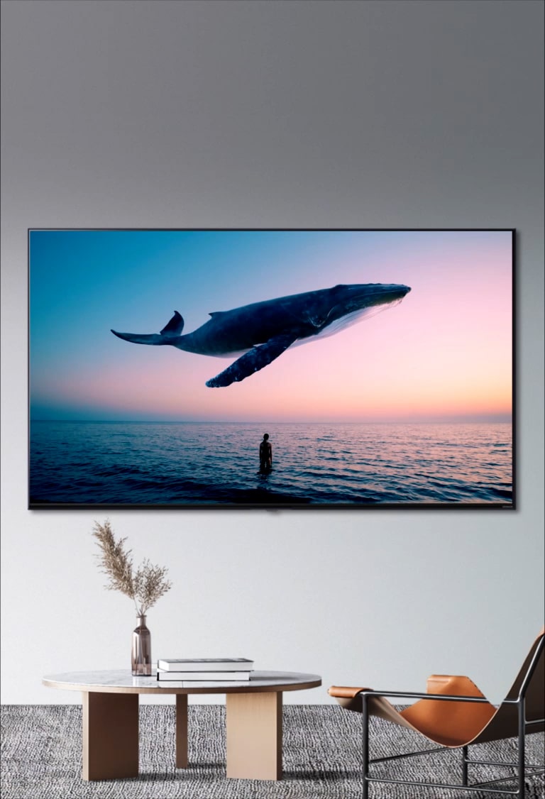 Big whale and a woman is diaplayed in the TV, which is hanging on the wall in the room with orange single sofa and round table. 