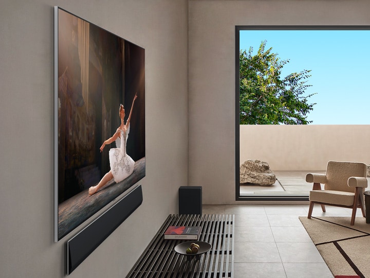 Széles látószögű nézet egy nappaliról egy luxusotthonban, ahol egy pár filmet néz a falra szerelt LG OLED TV-n. A TV kialakítása elegánsan beleolvad a falba és a belső dizájnba.
