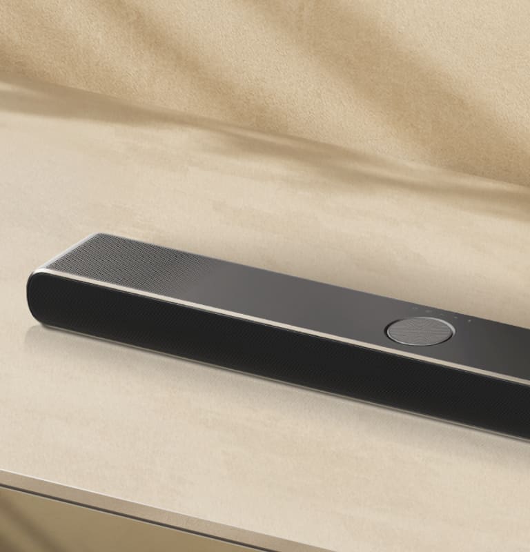 LG Soundbar bézs színű felületen, bézs színű háttér előtt, légi perspektívában.