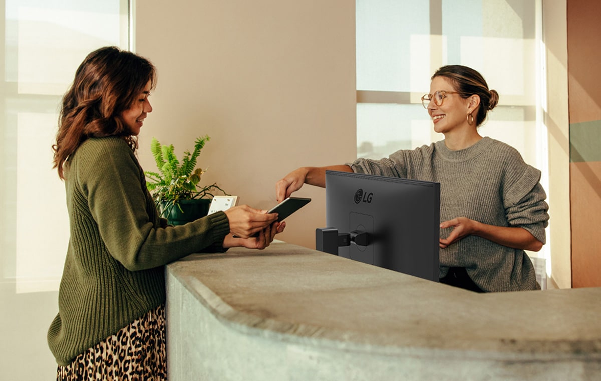 Barátságos recepciós mutatja egy hölgynek, hogy hol kell aláírni egy digitális táblagépen.