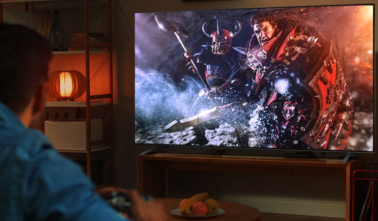 Seorang pria duduk di sofa dalam ruangan gelap dan bermain game RPG di TV besar. 