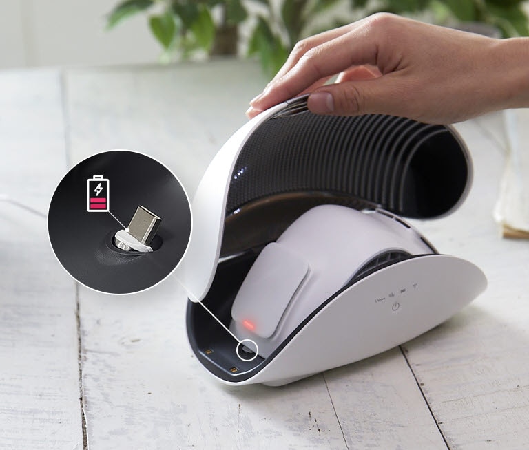 Bagian depan case Wearable Air Purifier dengan penutup terbuka dan tampak wearable air purifier didalamnya dengan latar belakang sebuah handphone yang layarnya menunjukkan ThinQ app dan ikon Wifi diatasnya