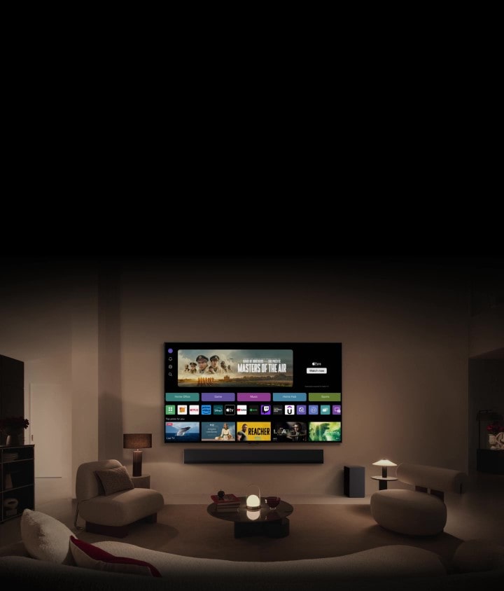 Tampilan dekat layar LG TV, yang menampilkan tombol Home Office, Game, dan Musik di atas banner Masters of the Air, diperkecil untuk menampilkan TV yang dipasang di dinding ruang tamu. Logo berikut ditampilkan di layar TV pada gambar: LG Channels, Netflix, Prime Video, Disney TV, Apple TV, YouTube, Spotify, Twitch, GeForce Now dan Udemy.