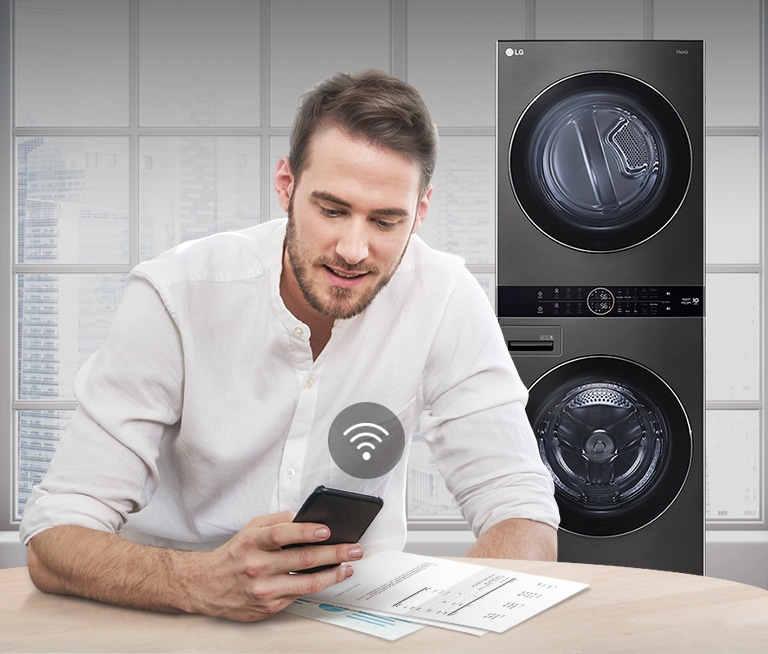 A man is monitoring the condition of the washing machine through a mobile phone app.