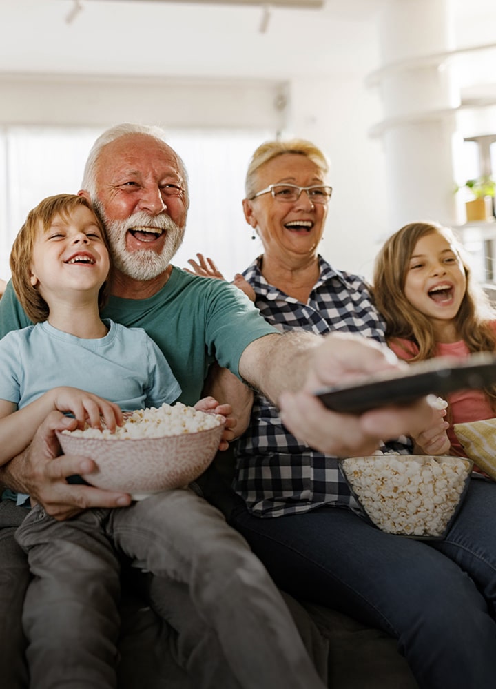 A family sits laughing while the grandfather points the remote outward.