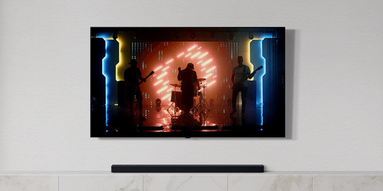 There is a TV and a soundbar in white living room. A group of band playing instruments and singing song on a TV screen. (play the video)