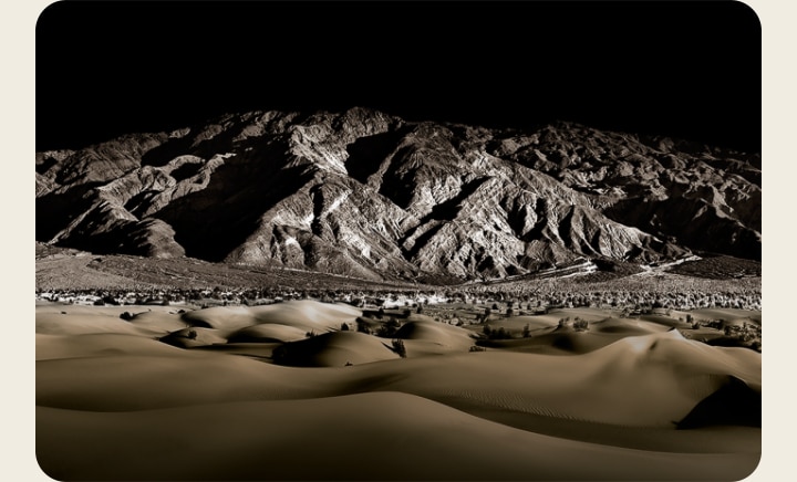 The words 'PERFECT BLACK' in white on a black background. A well-lit rocky mountain range appears in front, then moves upwards to reveal the landscape below as the words 'PERFECT BLACK' fade away.	