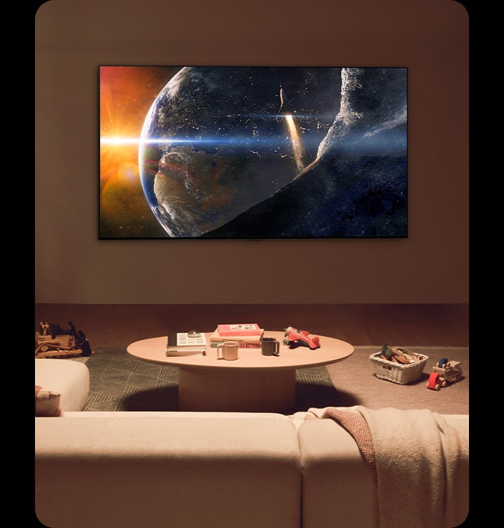 Una famiglia seduta sul pavimento di un soggiorno poco illuminato accanto a un tavolino mentre guarda un TV LG montato sul muro su cui si vede la terra dallo spazio.