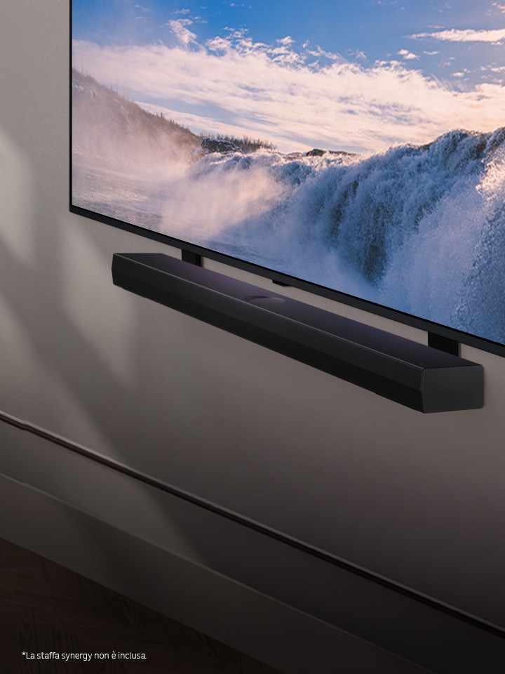 Una LG TV e una Soundbar sono posizionate all’interno di una prospettiva angolata montata su una parete. Sulla TV si vede il primo piano di una vasta cascata e una morbida cascata di luce solare sul muro, sulla TV e sulla Soundbar. L’esclusione di responsabilità recita: “La staffa Synergy viene fornita con un supporto unipolare o bipolare, che può variare in base al paese/prodotto”.