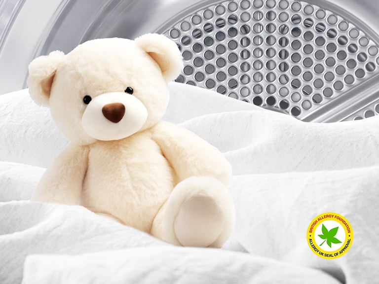 Immagine di una coperta e di un orsacchiotto all'interno di un'asciugatrice LG con il logo della British Allergy Foundation visualizzato