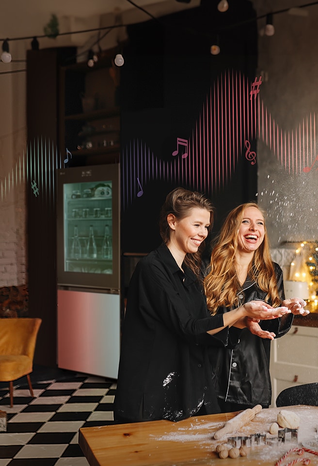 L'immagine di due donne ad una festa in una cucina con dietro un frigorifero illuminato.