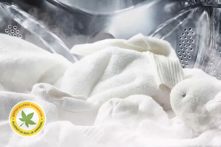 Immagine che mostra il lavaggio con vapore di una maglia morbida bianca e un animale di pelouche all'interno della lavatrice.