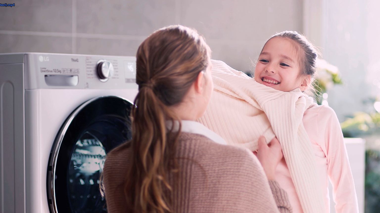 Maglioni infeltriti come rimediare: immagine di una mamma che aiuta la sua bambina a indossare un maglione di lana vicino ad una lavatrice LG. 