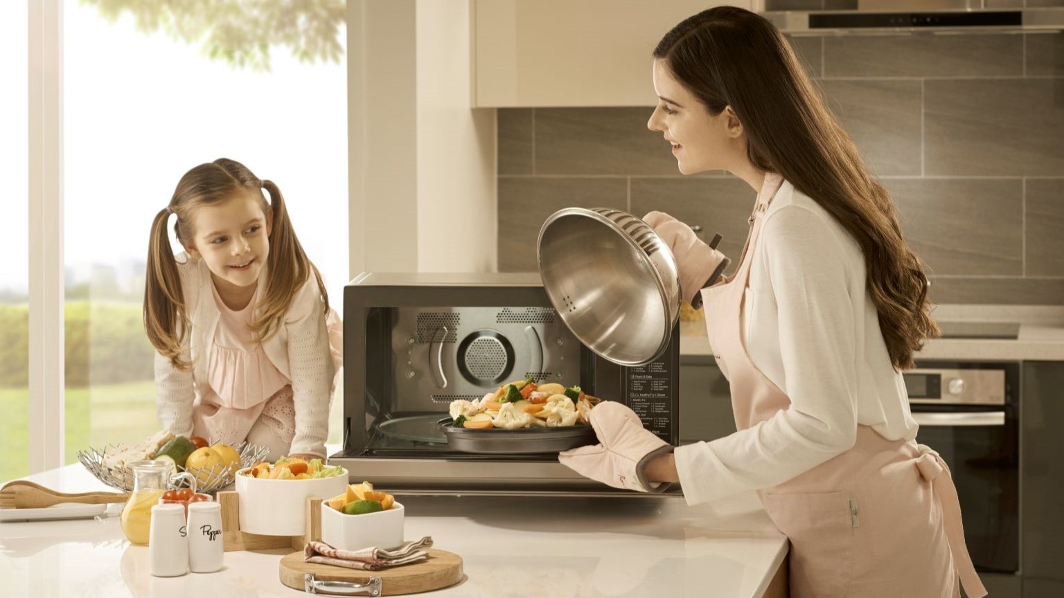 Come cuocere a vapore: immagine di una mamma e una bambina che cuociono verdure a vapore nel microonde.      