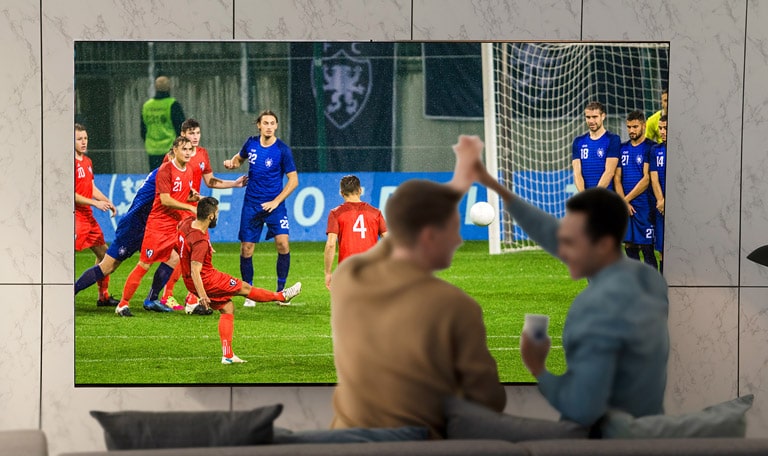 Persone in soggiorno che guardano una partita su un TV di grandi dimensioni.