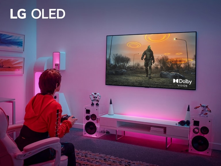 Una persona seduta su una sedia da gaming, che gioca su un TV OLED LG con Dolby Vision. La stanza presenta un design elegante e futuristico con illuminazione ambientale rosa e blu.