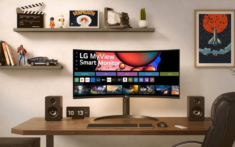 Smart monitor LG su scrivania moderna, con altoparlanti e orologio. Sullo sfondo si trova una parete decorata con mensole, quadri e soprammobili che donano eleganza alla postazione di lavoro.