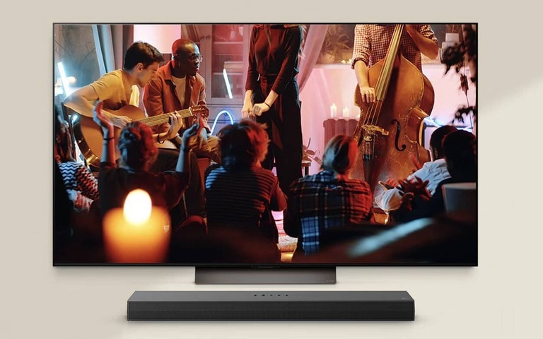 Un TV LG che mostra un’esibizione di musica dal vivo, in cui dei musicisti suonano la chitarra e il contrabbasso in un ambiente con illuminazione calda. Al di sotto del TV LG si trova una soundbar LG, che rende la scena ancora più immersiva