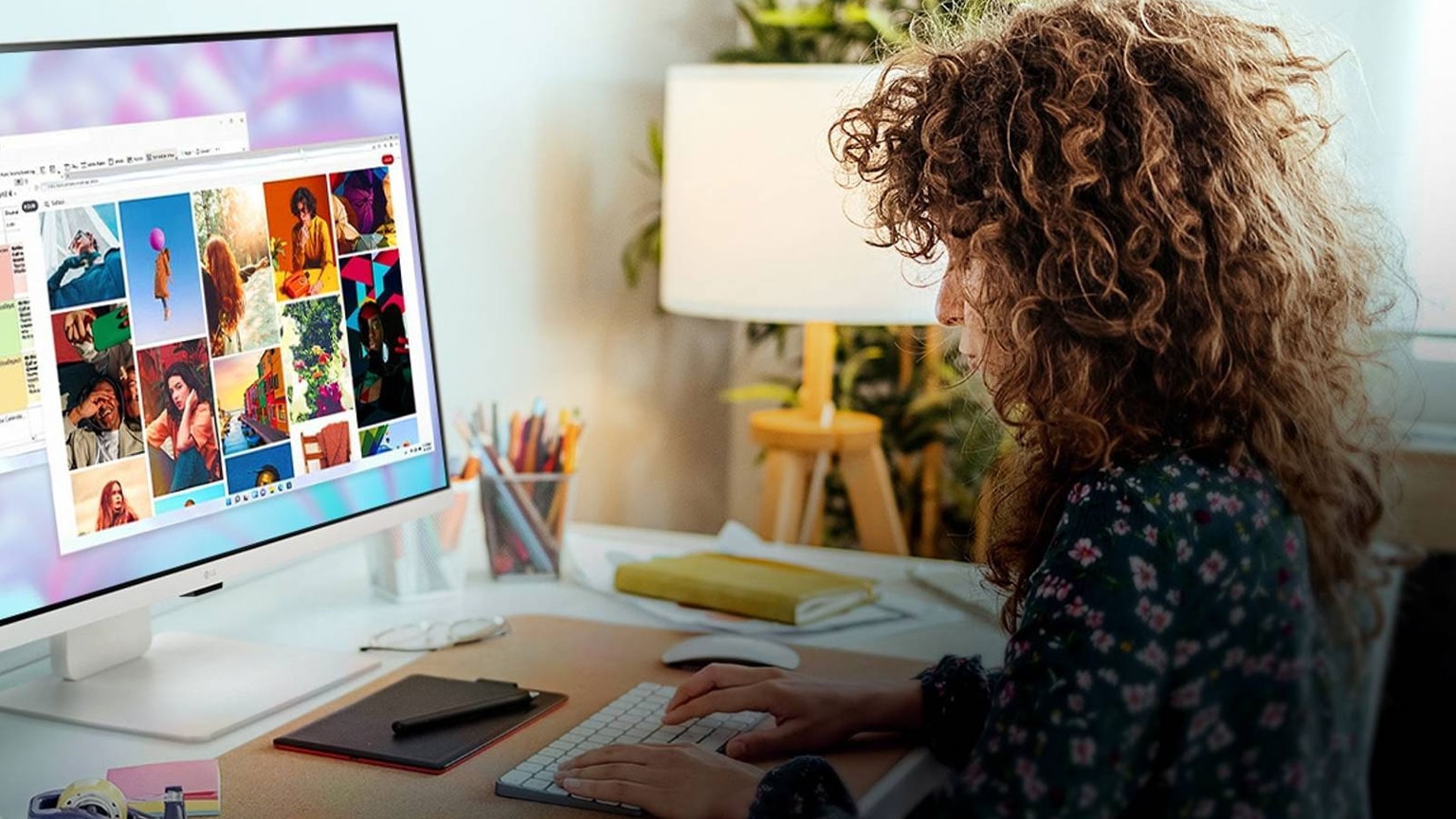 Una persona lavora davanti a uno smart monitor LG, in cui sono visualizzati documenti e immagini. La postazione di lavoro, in un accogliente studio domestico, include una pianta, una lampada e quaderni.