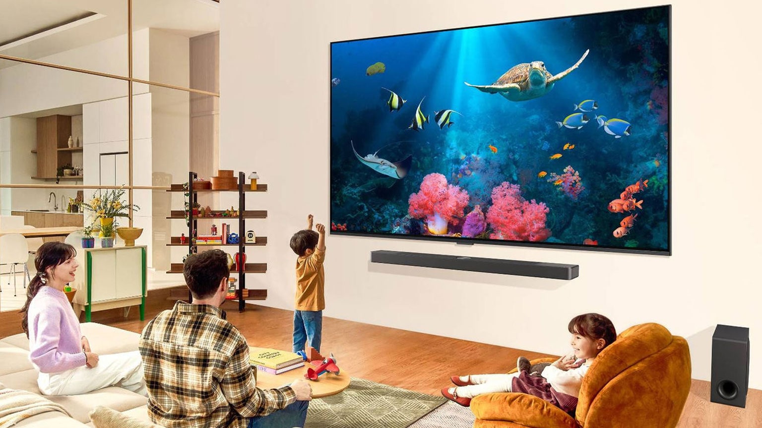 Una famiglia in un soggiorno che guarda una scena sottomarina con coralli e creature marine dai colori accessi su un TV LG montato a parete. Sotto il TV LG si trovano una soundbar e un subwoofer LG che migliorano l’esperienza visiva all’interno del soggiorno spazioso e moderno.