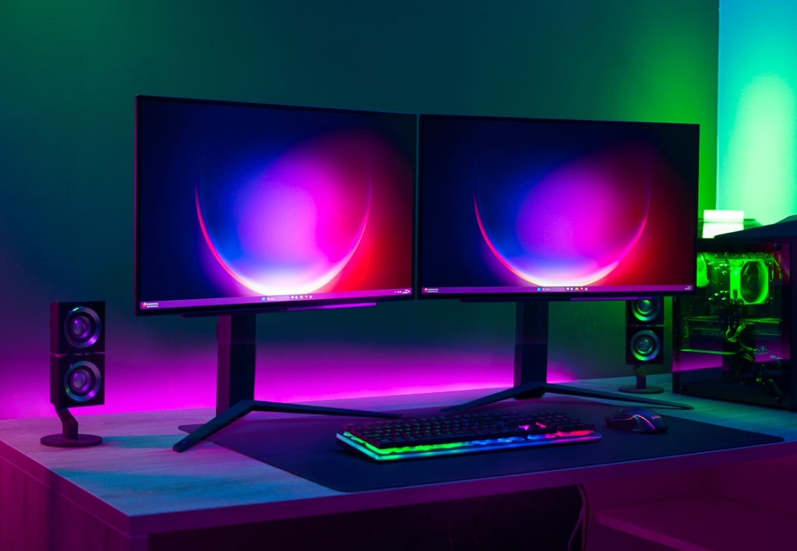 Setup a doppio monitor con illuminazione LED colorata, che mostra una tastiera e un mouse sulla scrivania.