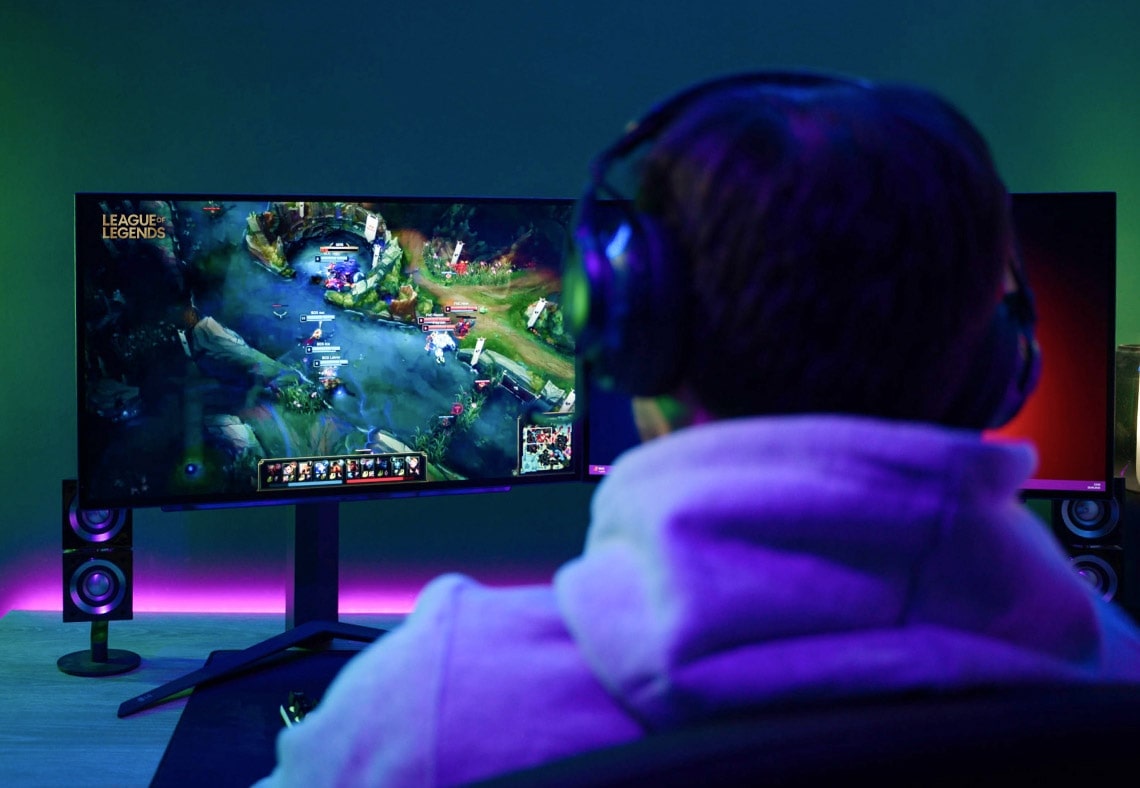 Un giocatore visto di spalle, che gioca su un setup a doppio monitor con illuminazione LED.
