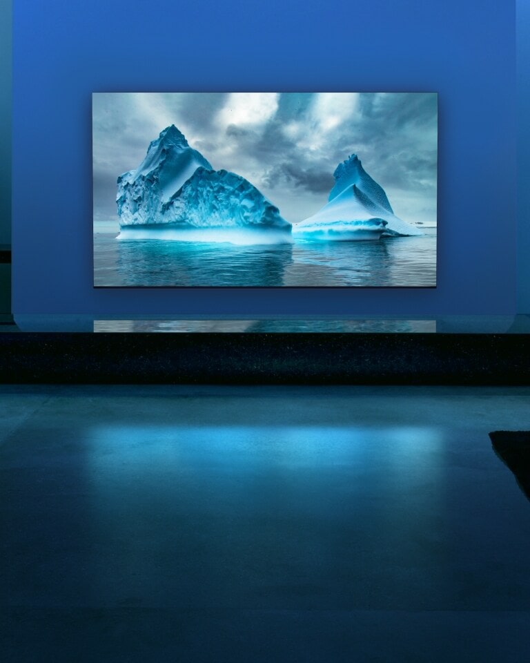 青色のネオン回路が青色の氷河の画像上を動き回ります。カメラがズームアウトし、この青色の氷河をテレビ画面の中に映し出します。テレビは広いリビングルームに置かれていて、背景は青色です。 