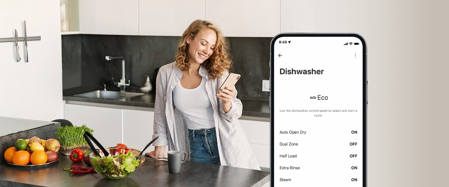 Женщина смотрит на свой мобильный телефон на кухне, а на смартфоне показаны настройки персонализации в приложении ThinQ™. 	