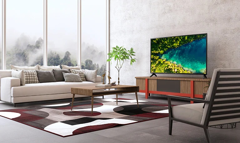 Телевизор, на экране которого показан вид сверху на густой лес, в котором стоит современный и простой дом.