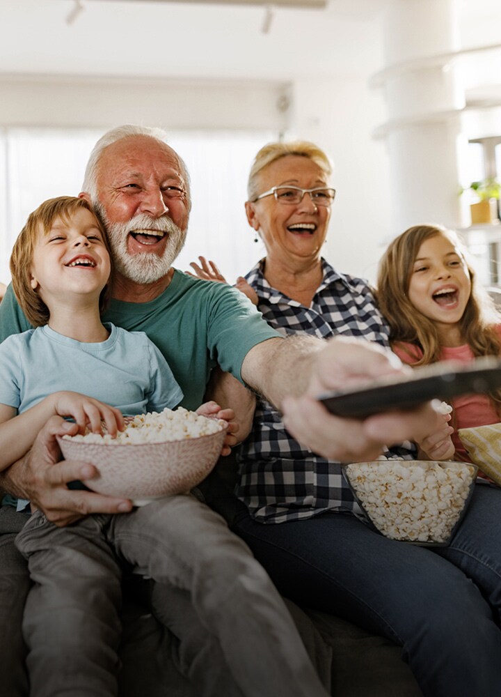 Una familia se sienta a reír mientras el abuelo apunta el control remoto hacia afuera.