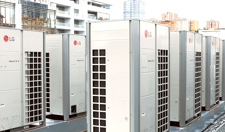 Vista frontal lateral de una serie de unidades LG Multi V 5, con la mitad derecha cubierta por conductos de ventilación cuadriculados, alineadas en el techo del edificio.